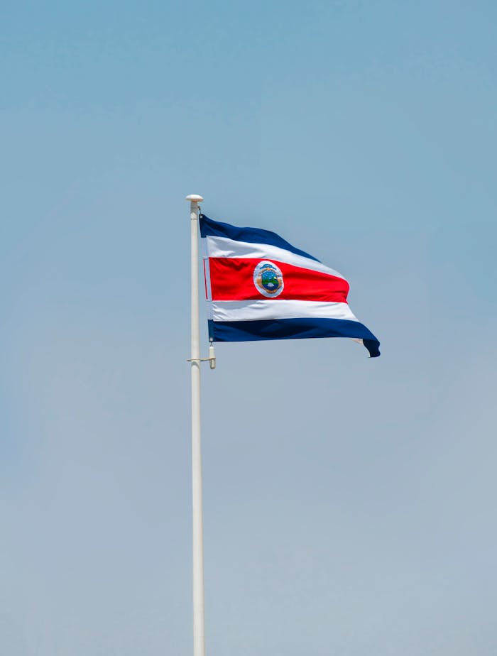 Costa Rican national flag gracefully swaying on a flagpole against a clear blue sky.
